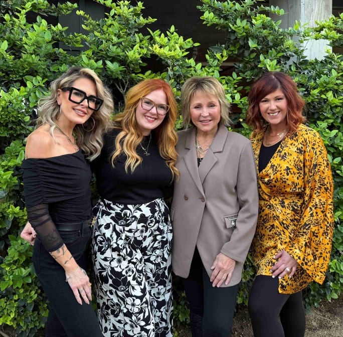 Four women elegantly dressed in front of a tree.