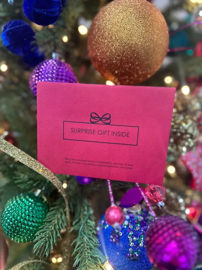 Red envelope labeled “Surprise Gift Inside” displayed on a decorated holiday tree, representing a salon retention program designed to drive rebooking in slower months.