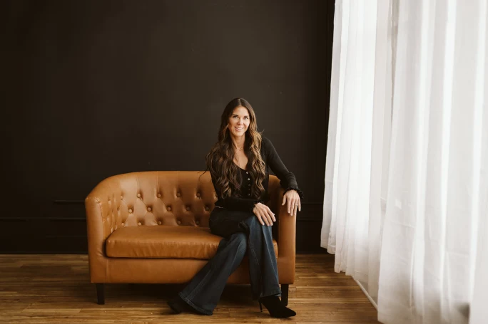 Kati Whitledge sits on a brown couch with daylight illuminating her face