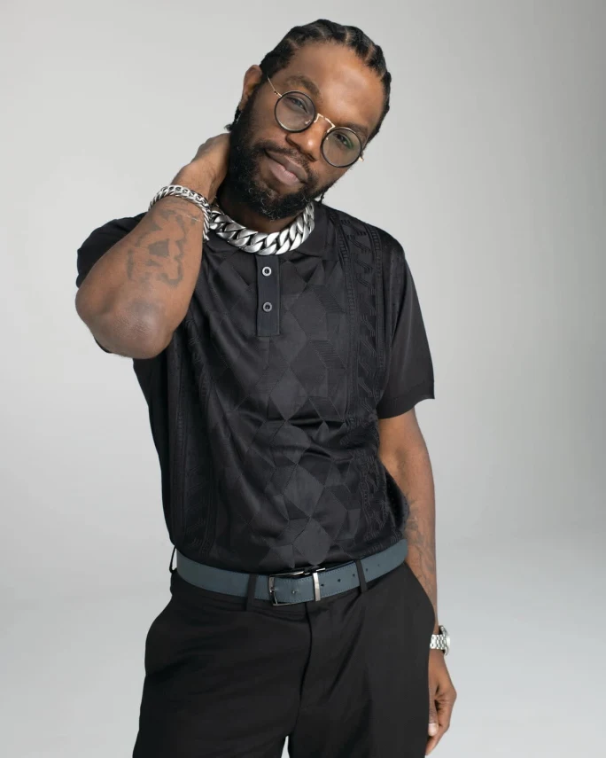A man wearing all black, his hand to his neck.