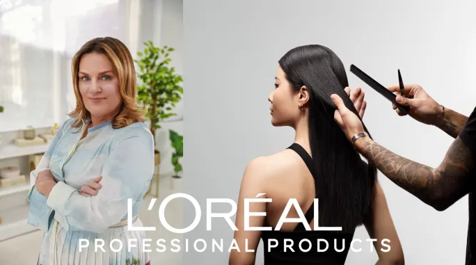 A woman with crossed arms and a model having her hair brushed by a hairstylist