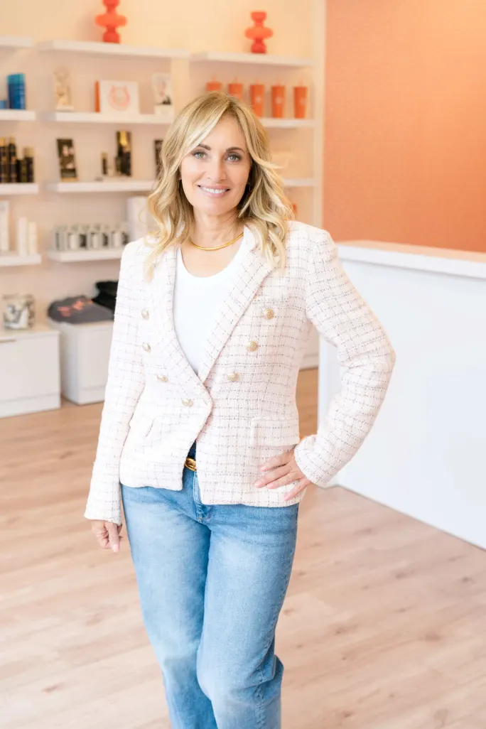 In a chic pink jacket, Owner Lia Hakim poses in front of the retail wall at Hott Salons.