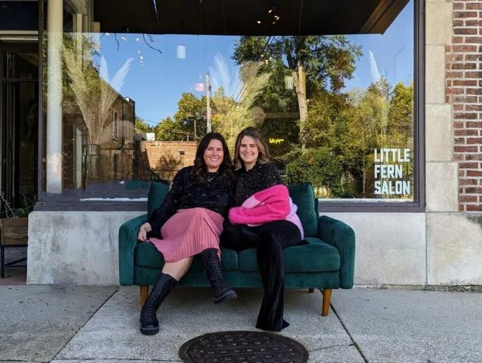 Two women pose on a couch outside Little Fern Salon.