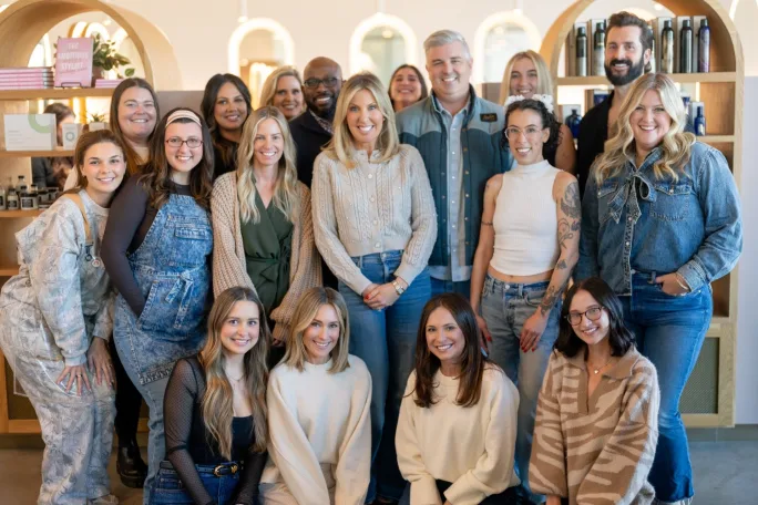 A large group of stylists pose in the pale pink Mirror Mirror Salon.