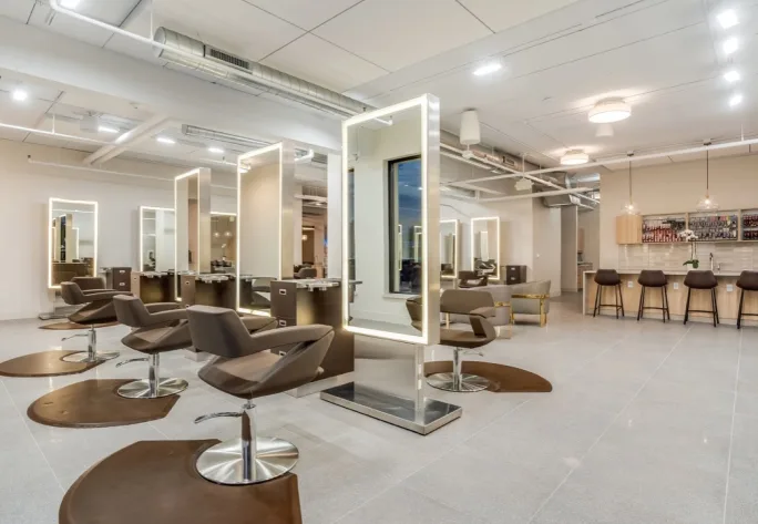 A color bar is in the backgroud with double-sided hair stations and brown salon chairs in Neroli Salon.