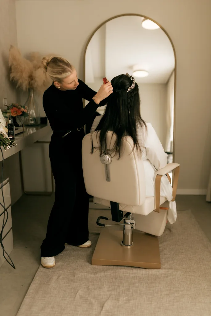 A stylist adjusts a woman's headpiece.