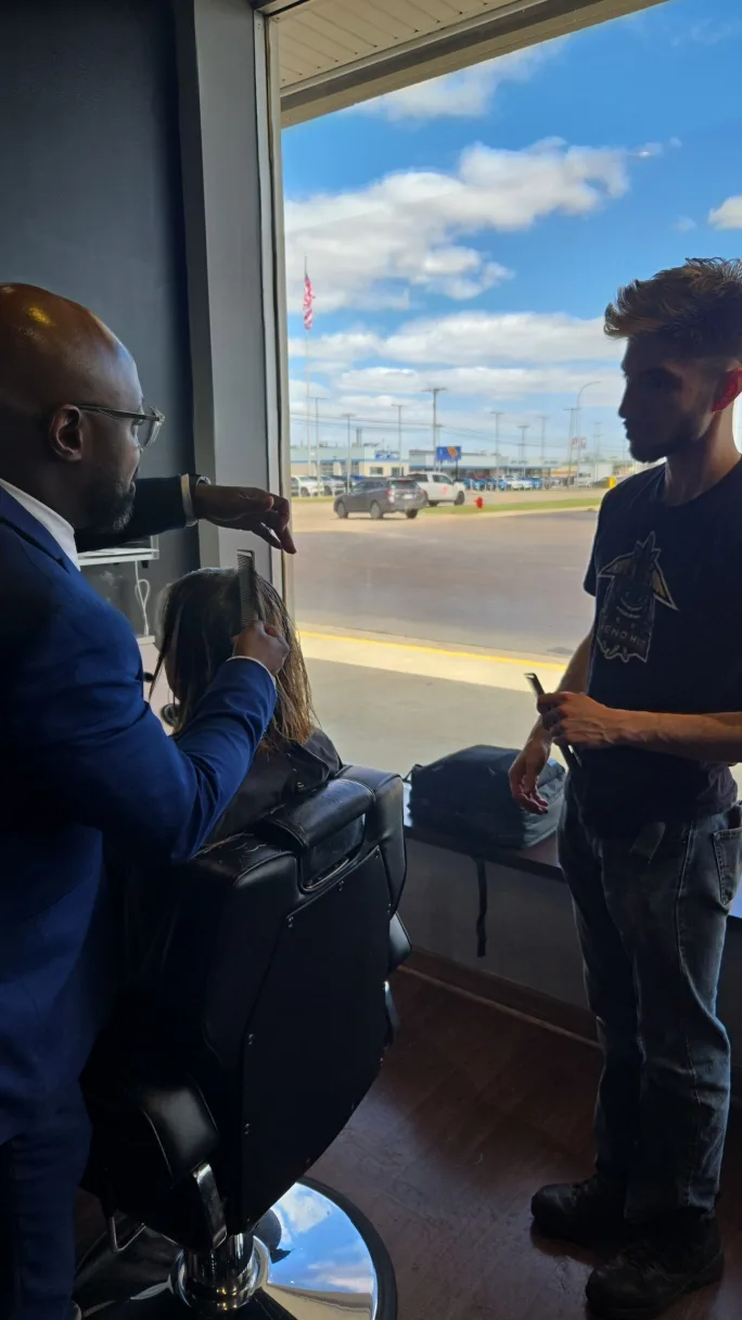 Barber educator mentoring a student while demonstrating proper cutting form.