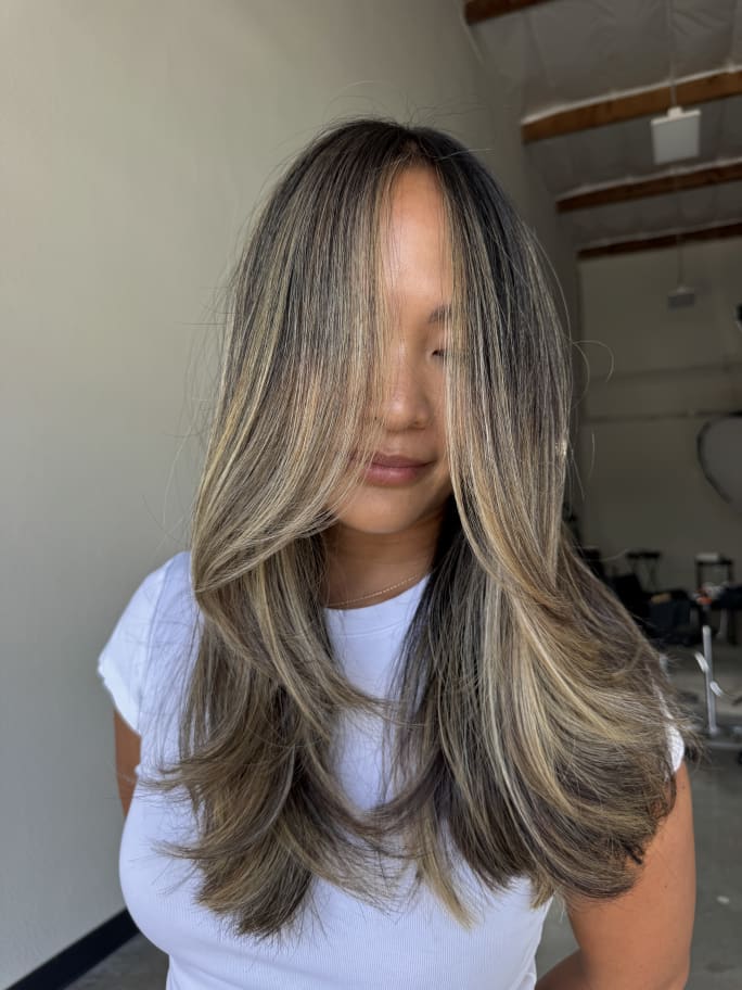 Young woman with long, softly waved hair featuring dimensional blonde highlights and a glossy finish.