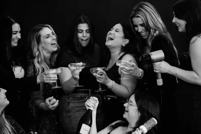 Holding glasses of champagne in a black and white image, the team from Something You Beauty