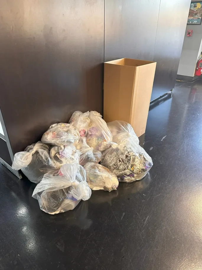 Bags of trash on the floor next to a cardboard collection box. 