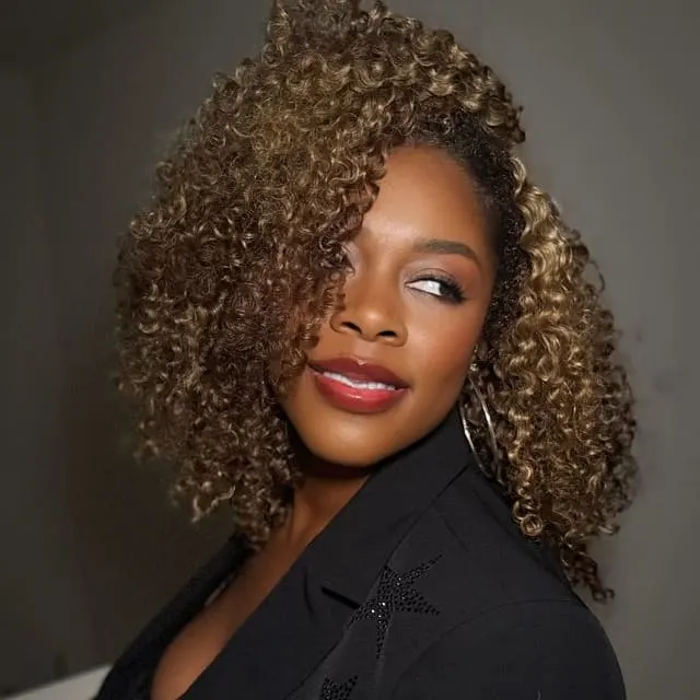 A woman in black, with tight, carmel curls,  looks over her shoulder.