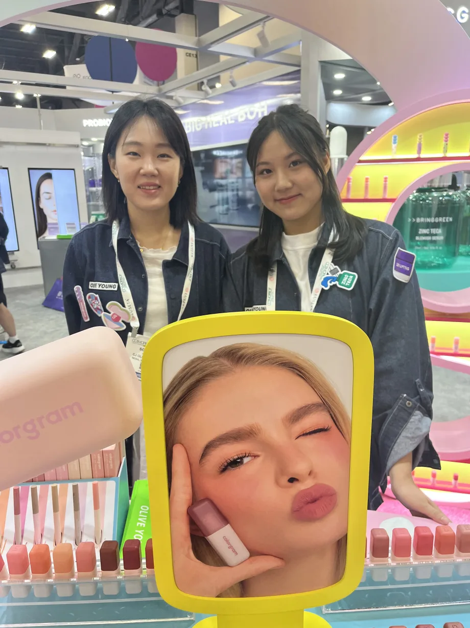 At the Olive Young booth at Cosmoprof North America, two women smile in front of a display.
