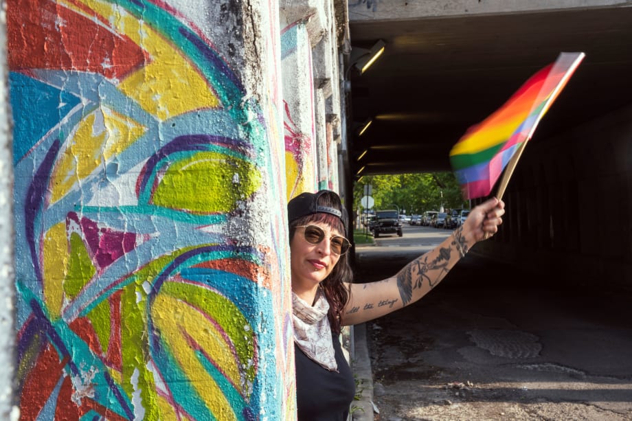 A woman holding a gay pride flag in front of a colorful mural.