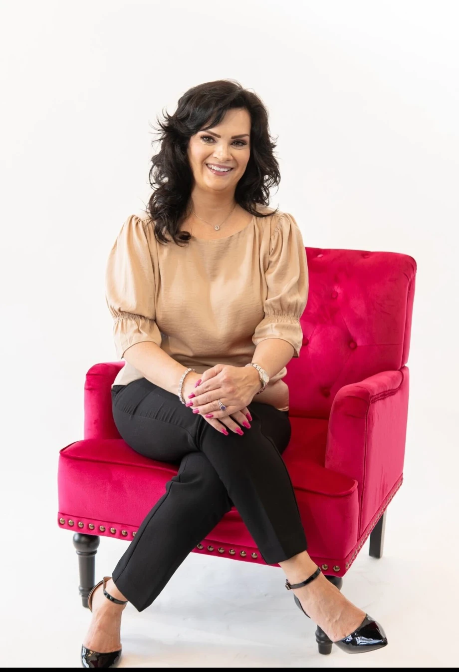 A woman seated, cross-legged, in a pink chair.
