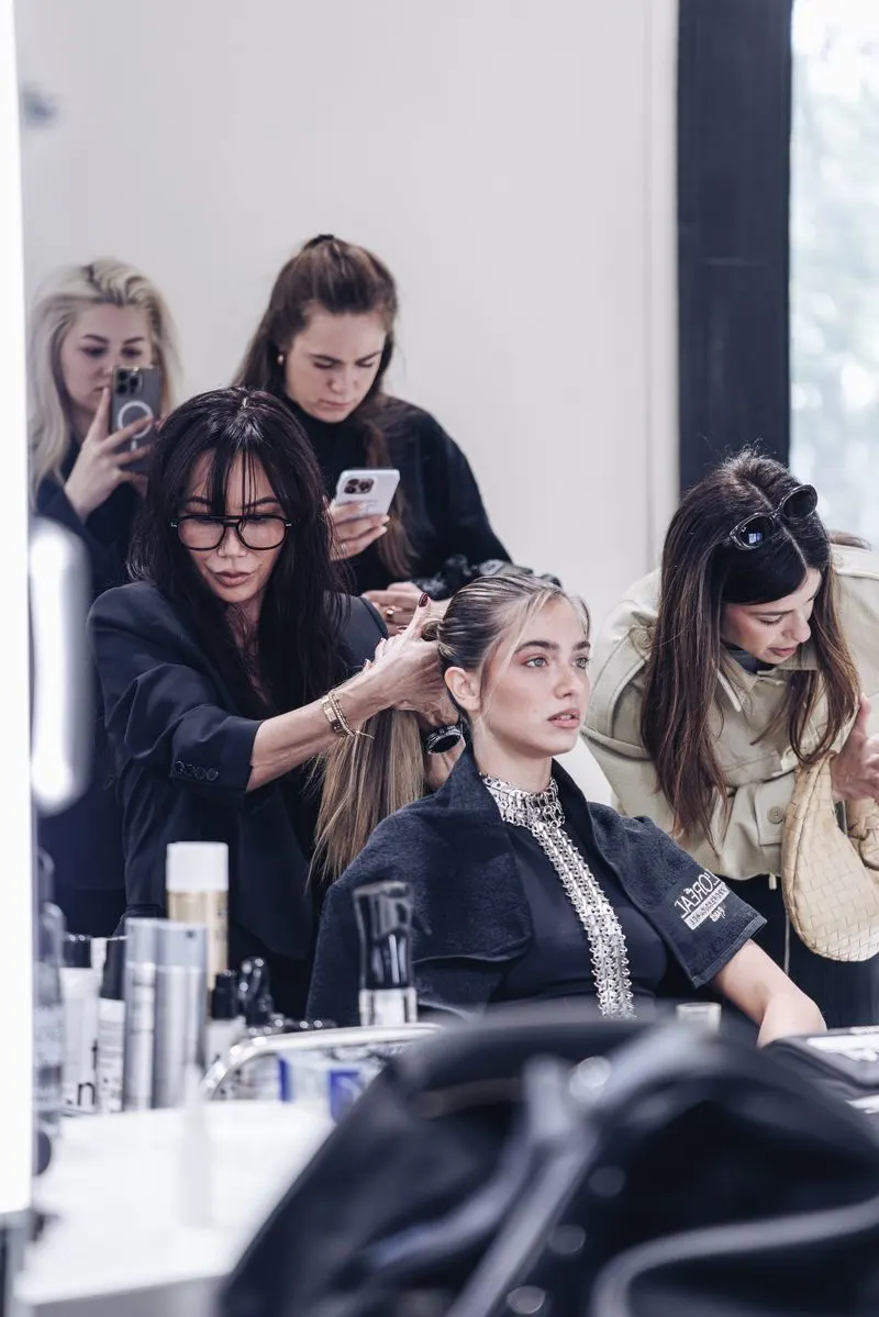 A stylist pulls a model's hair into a ponytail as influencers snap pictures with their iphones