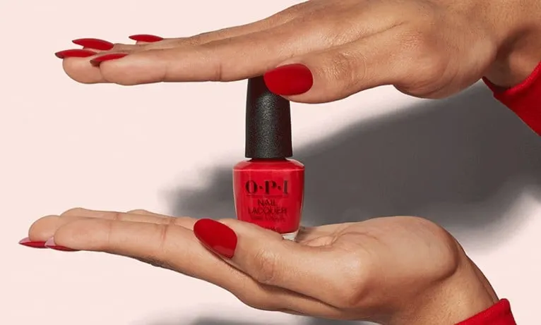 A pair of manicured hands holding a bottle of red nail polish