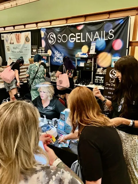 SO Gel Nails booth with owner Becky Bunnell standing on the right, engaging with attendees.